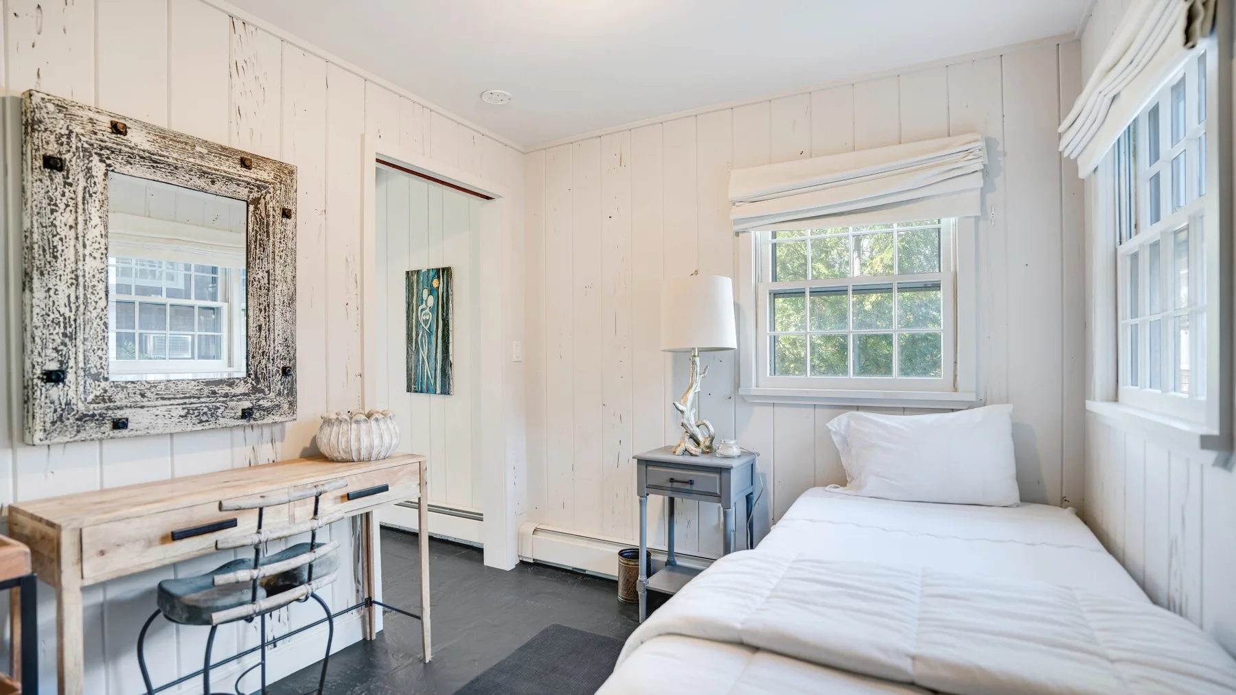 A bright bedroom with a bed, a desk, and large windows.
