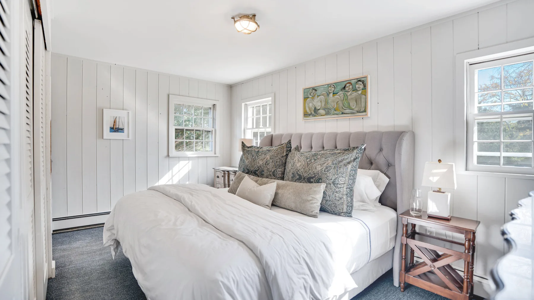 A bright bedroom with a large bed, white bedding, and windows.