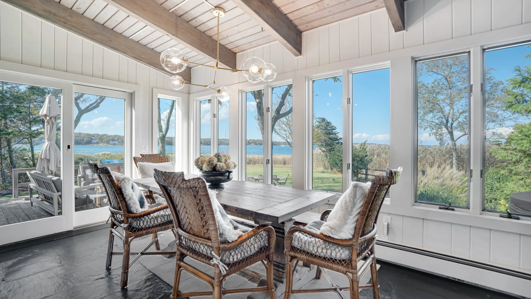 A bright dining area with a long table and woven seating beside large windows.