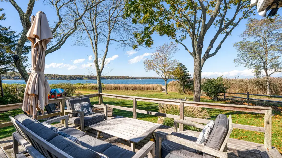 A wooden outdoor deck with cushioned seating overlooks a lake.