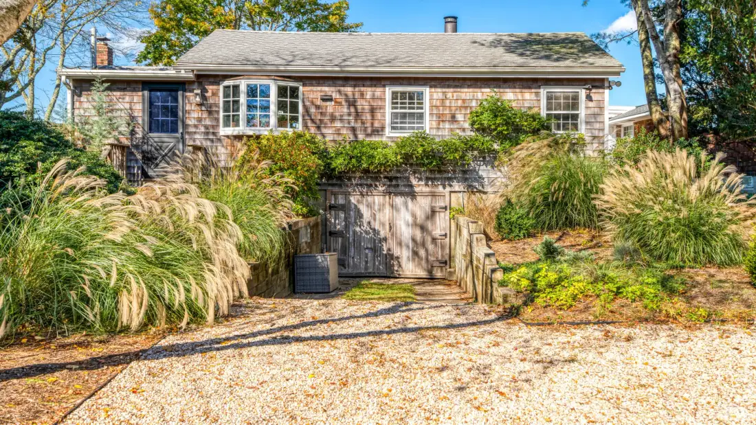 A shingled house stands behind ornamental grasses and a gravel path.