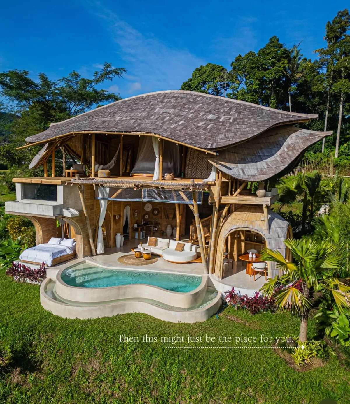 A distinctive open-air villa overlooks a curved swimming pool amid lush greenery.