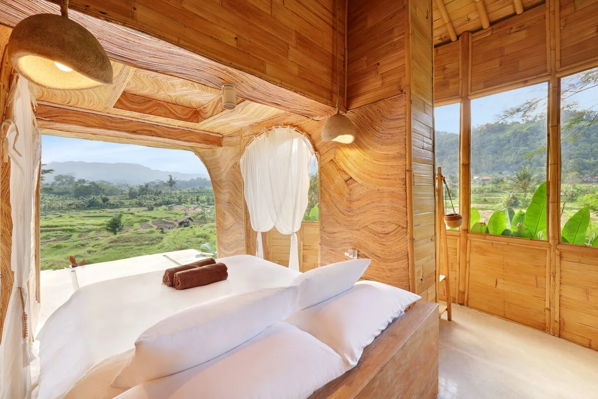 A bedroom with a bed beside large windows overlooking a green landscape.