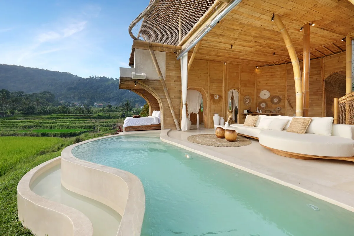 A curved pool sits beside an open-sided wooden lounge overlooking green fields.