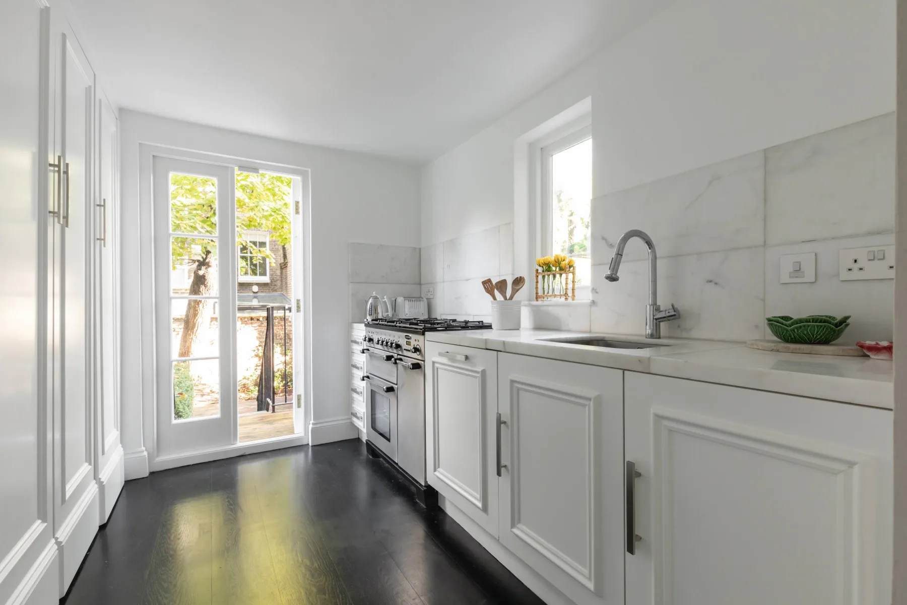 Una cocina blanca y luminosa con una encimera larga y puertas acristaladas.
