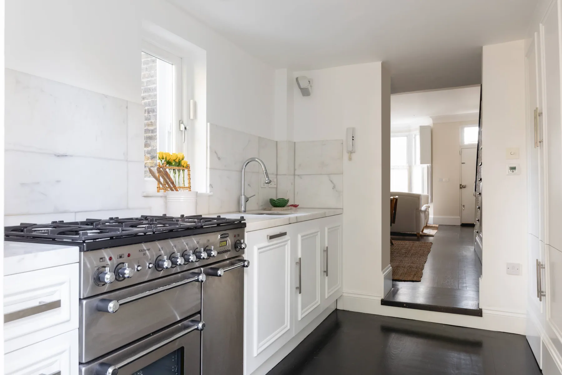 Una cocina luminosa con estufa, fregadero y una puerta hacia otra habitación.