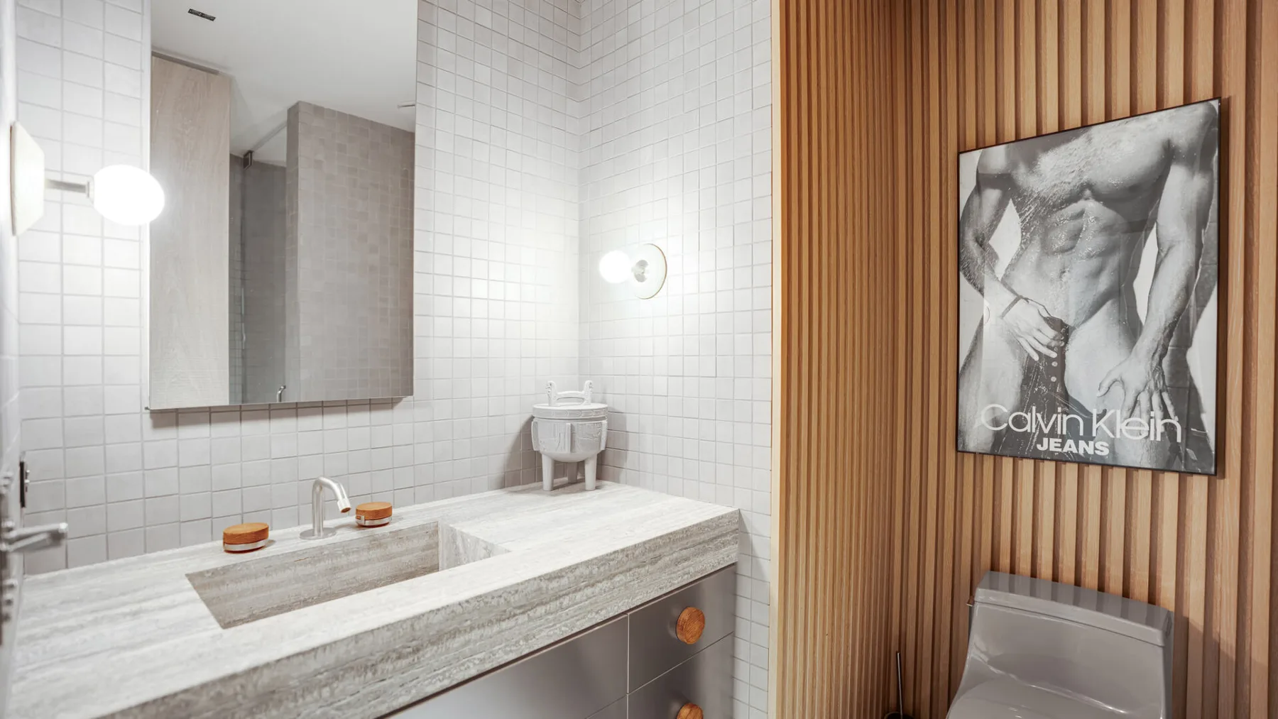 Un lavabo de baño con azulejos está junto a una pared revestida de madera con arte enmarcado.