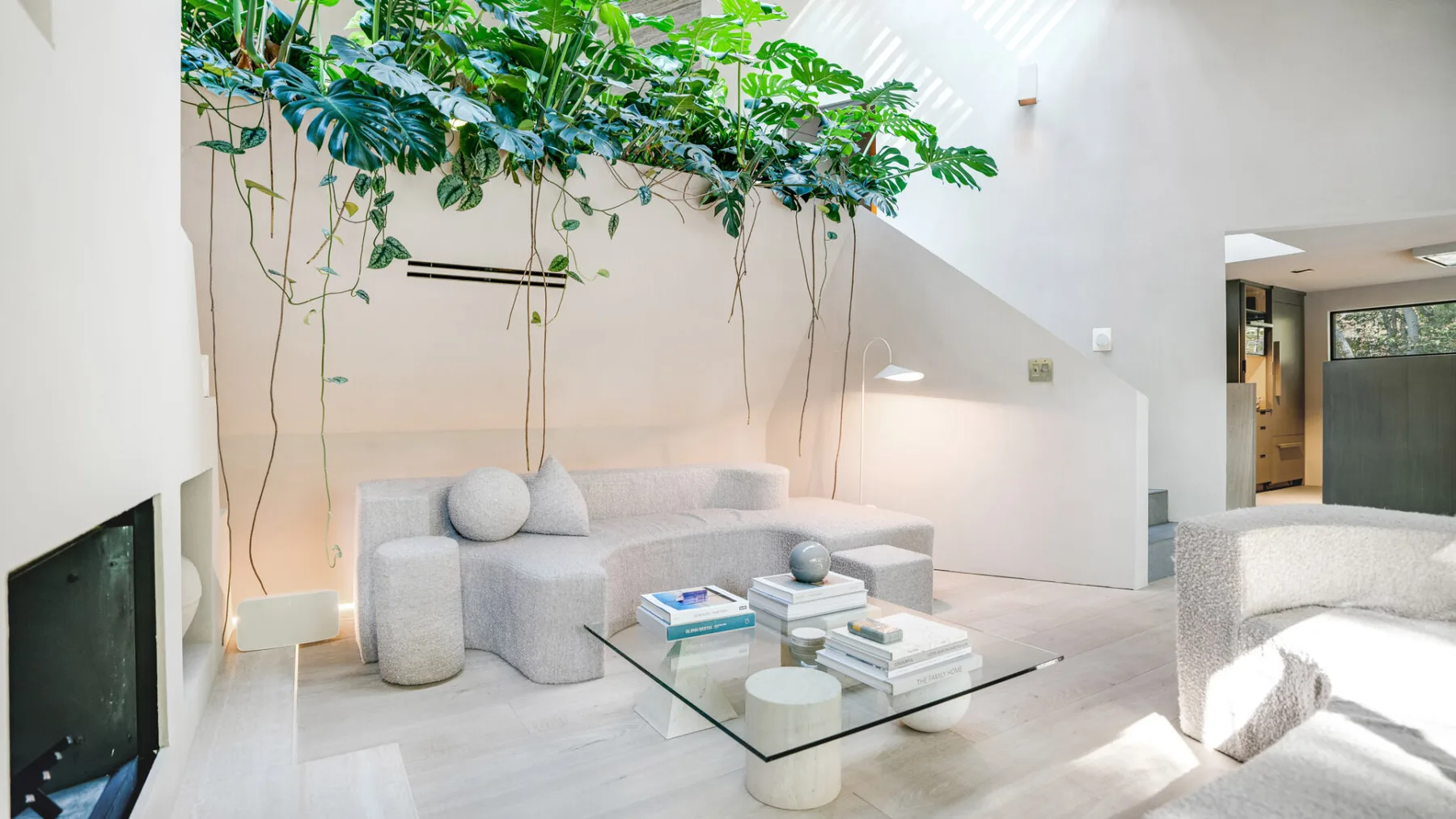 Una sala luminosa con asientos claros, una mesa de centro de vidrio y plantas colgantes.