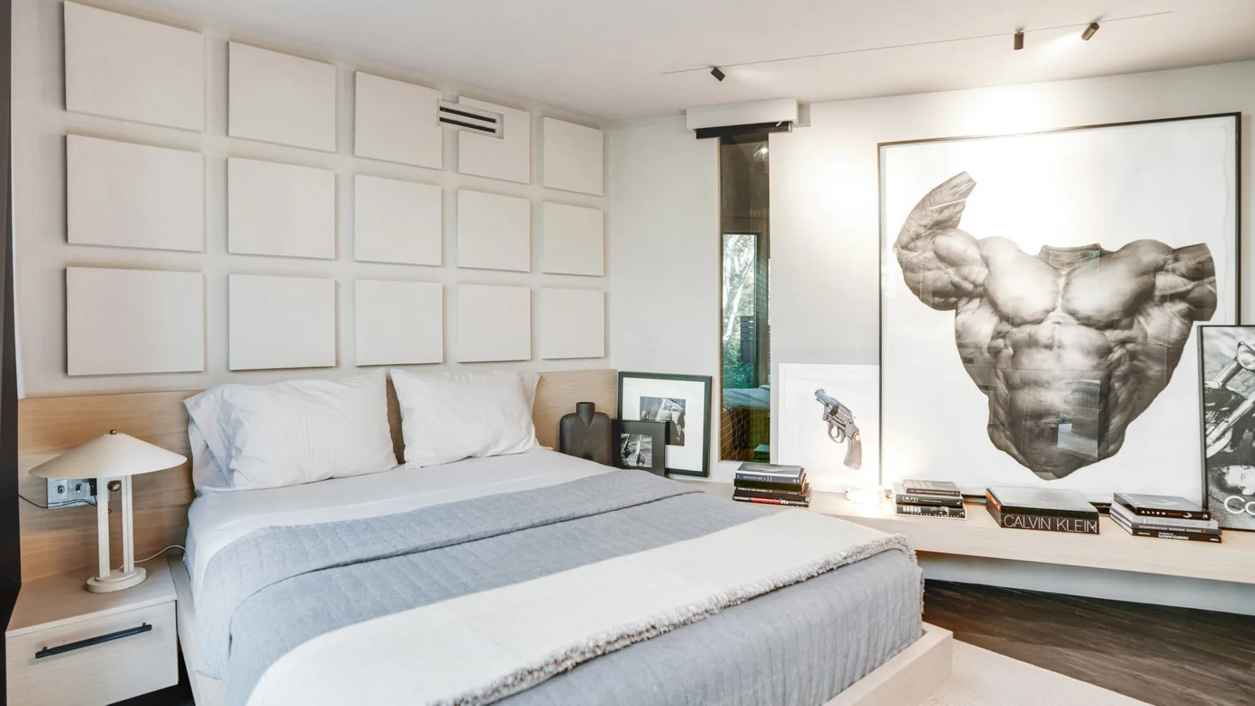 Un dormitorio con una cama bien tendida y una gran obra enmarcada en la pared.