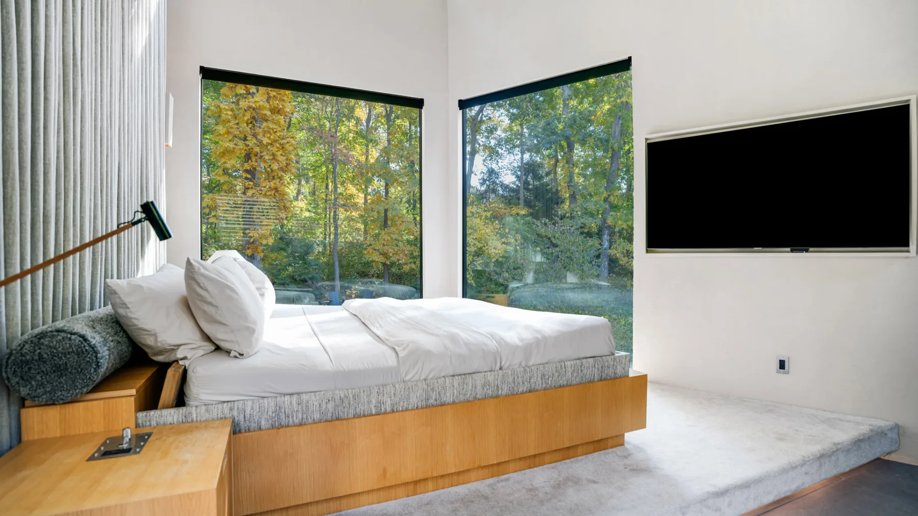 Un dormitorio con una cama baja junto a grandes ventanas con vista a los árboles.