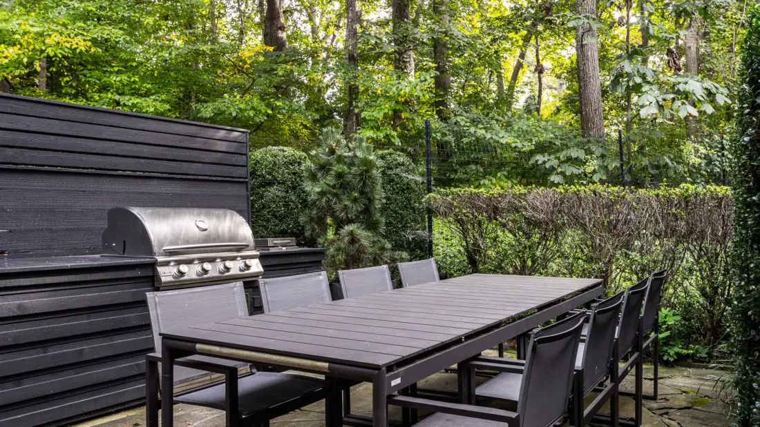 Una zona de comedor al aire libre con una mesa larga y sillas junto a una parrilla.