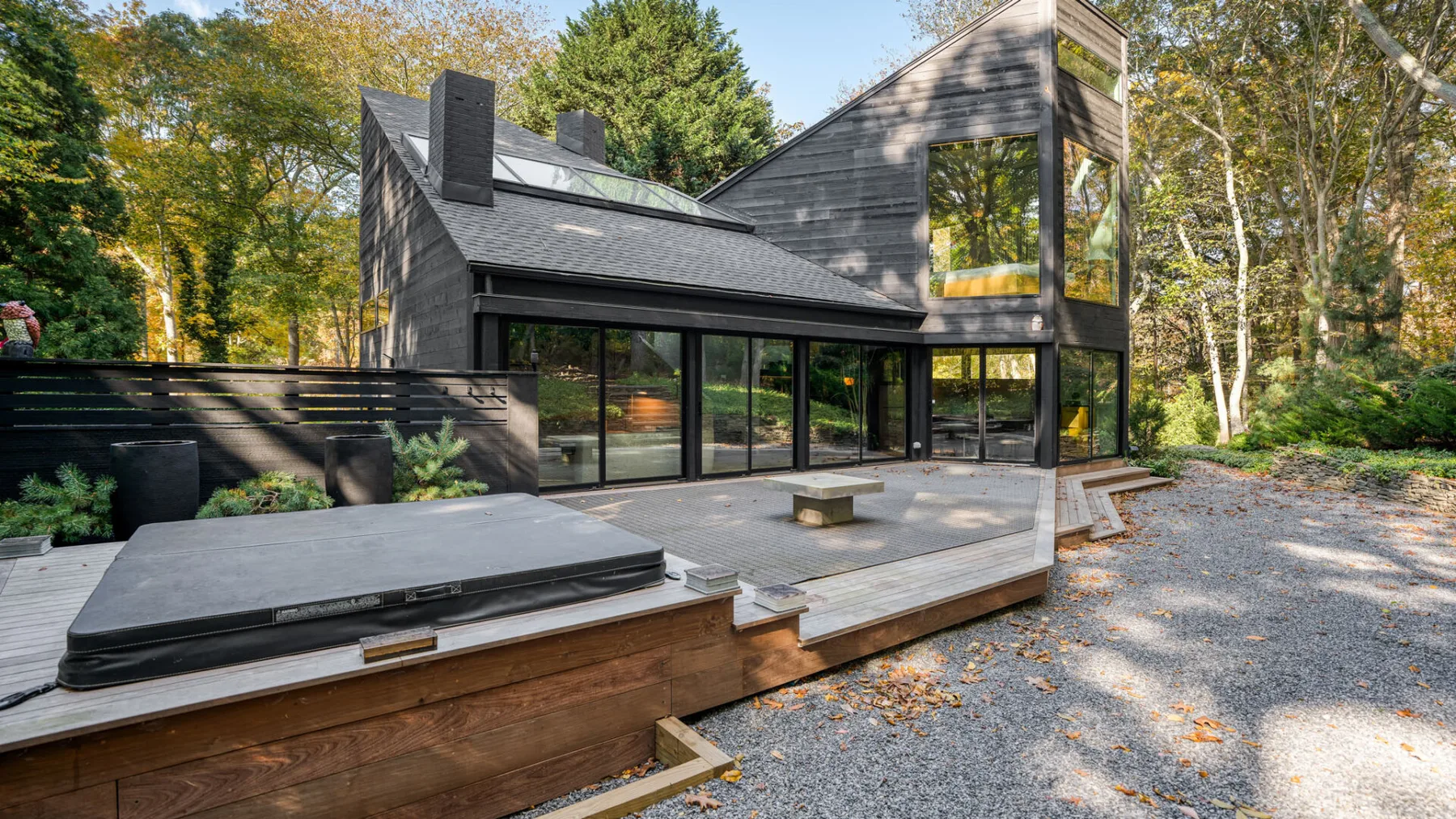 Una casa moderna y oscura da a una amplia terraza rodeada de árboles.
