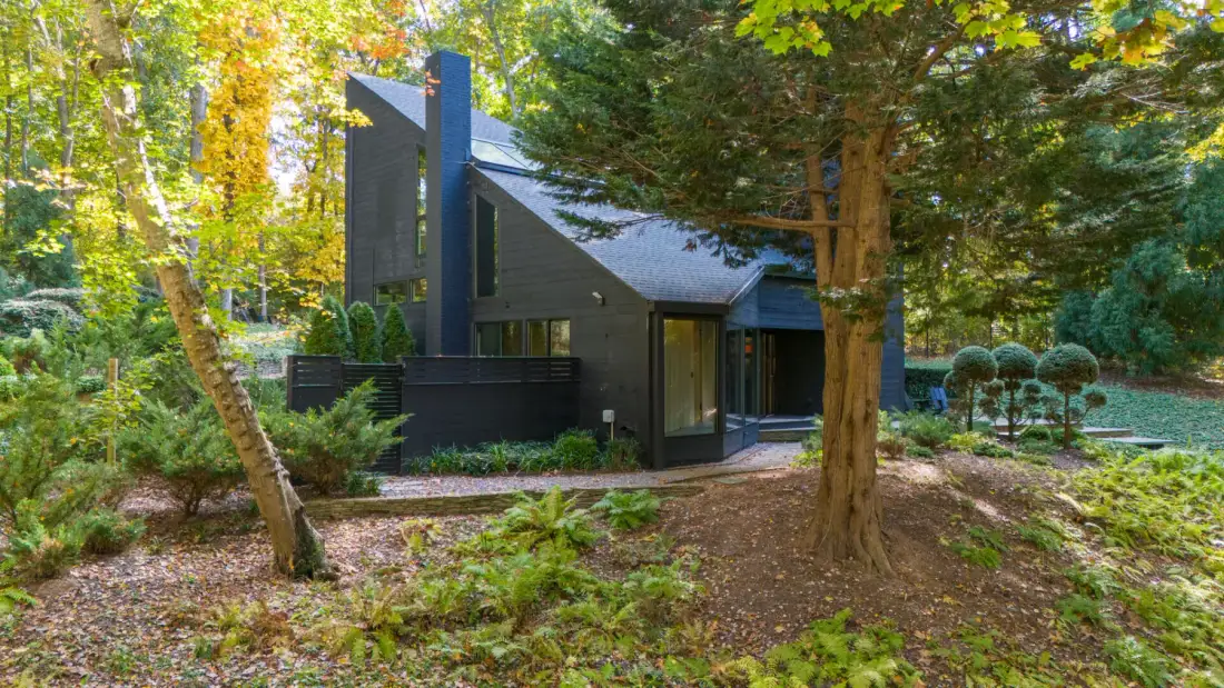 Una casa moderna oscura se encuentra entre árboles frondosos y vegetación ajardinada.