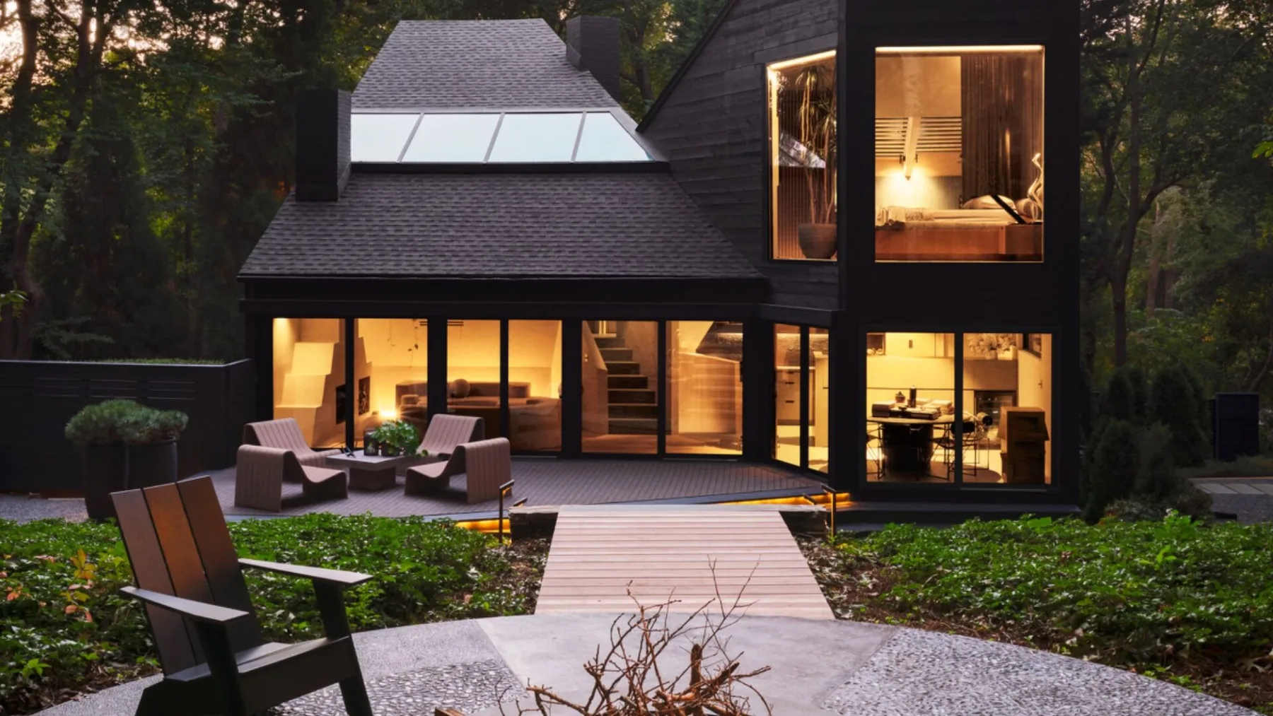 Una casa moderna con una terraza de madera y asientos al aire libre, rodeada de árboles.