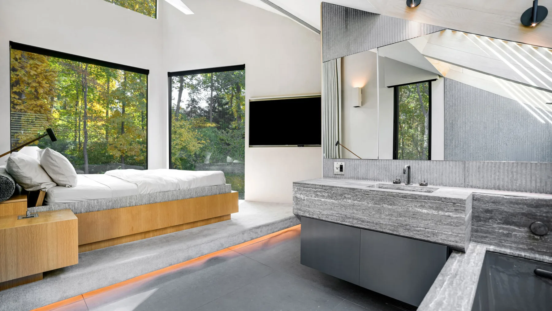 Un dormitorio luminoso con una cama junto a grandes ventanas y un tocador abierto.