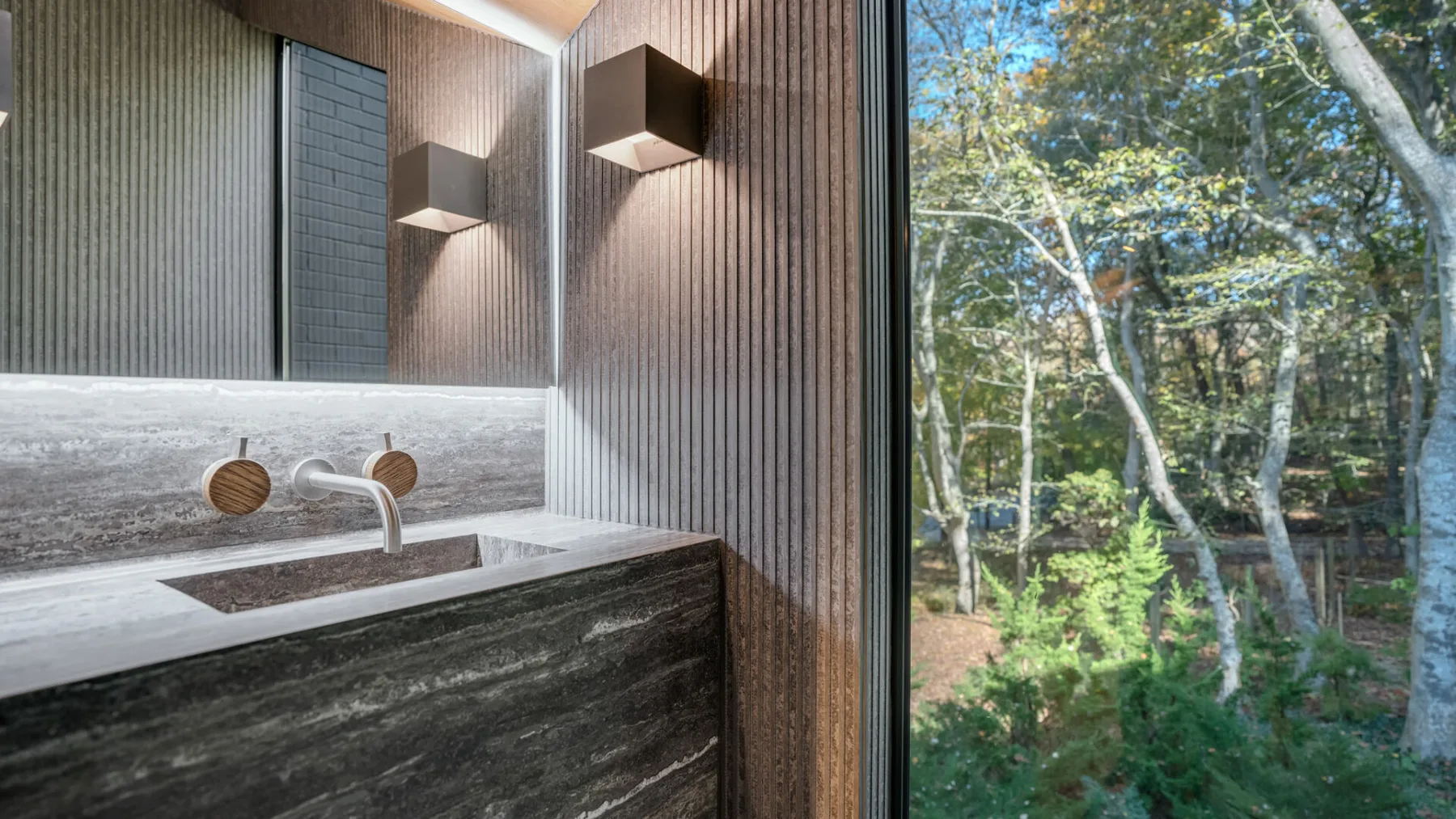 Un lavabo de baño con una pila rectangular está junto a una ventana amplia con vista a los árboles.