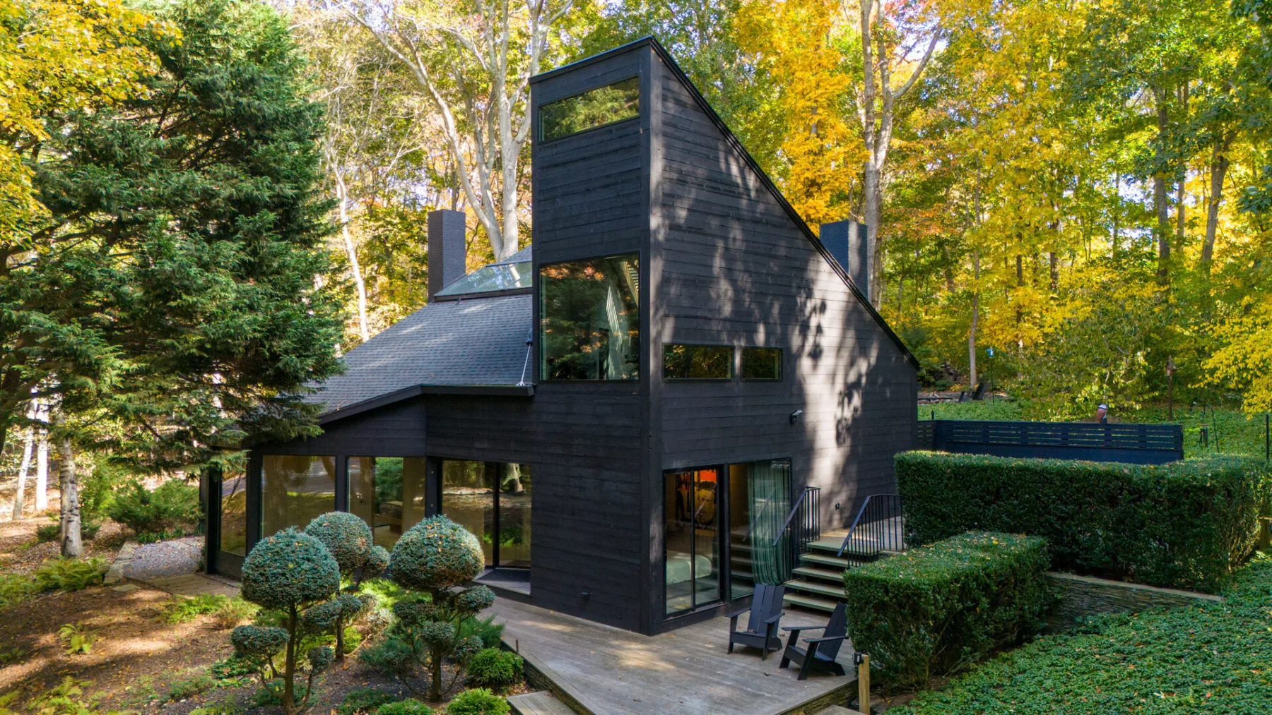 Una casa moderna de revestimiento oscuro está entre árboles, con un jardín cuidado.