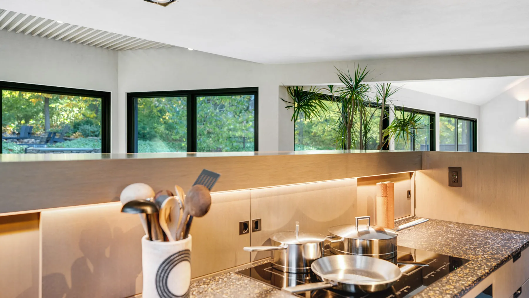 Una cocina moderna con placa de cocción, gabinetes de madera clara y ventanas grandes.