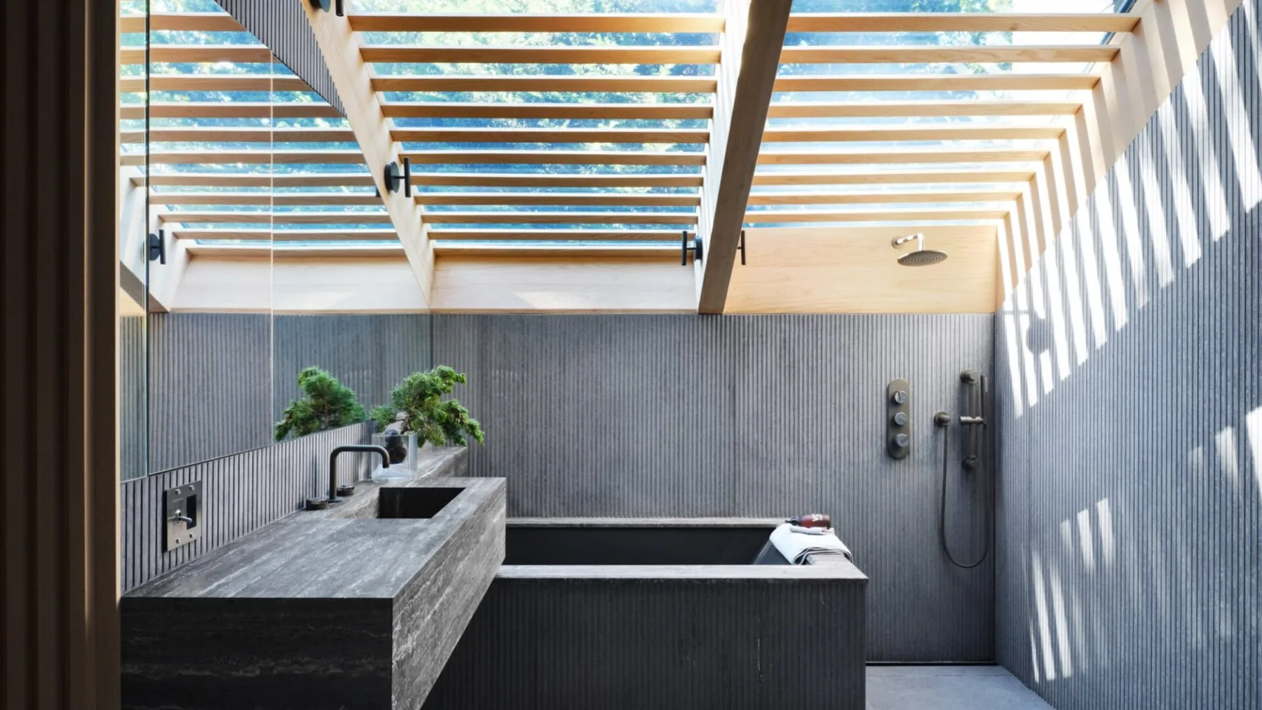 Un baño al aire libre con una bañera oscura y un lavabo de piedra.