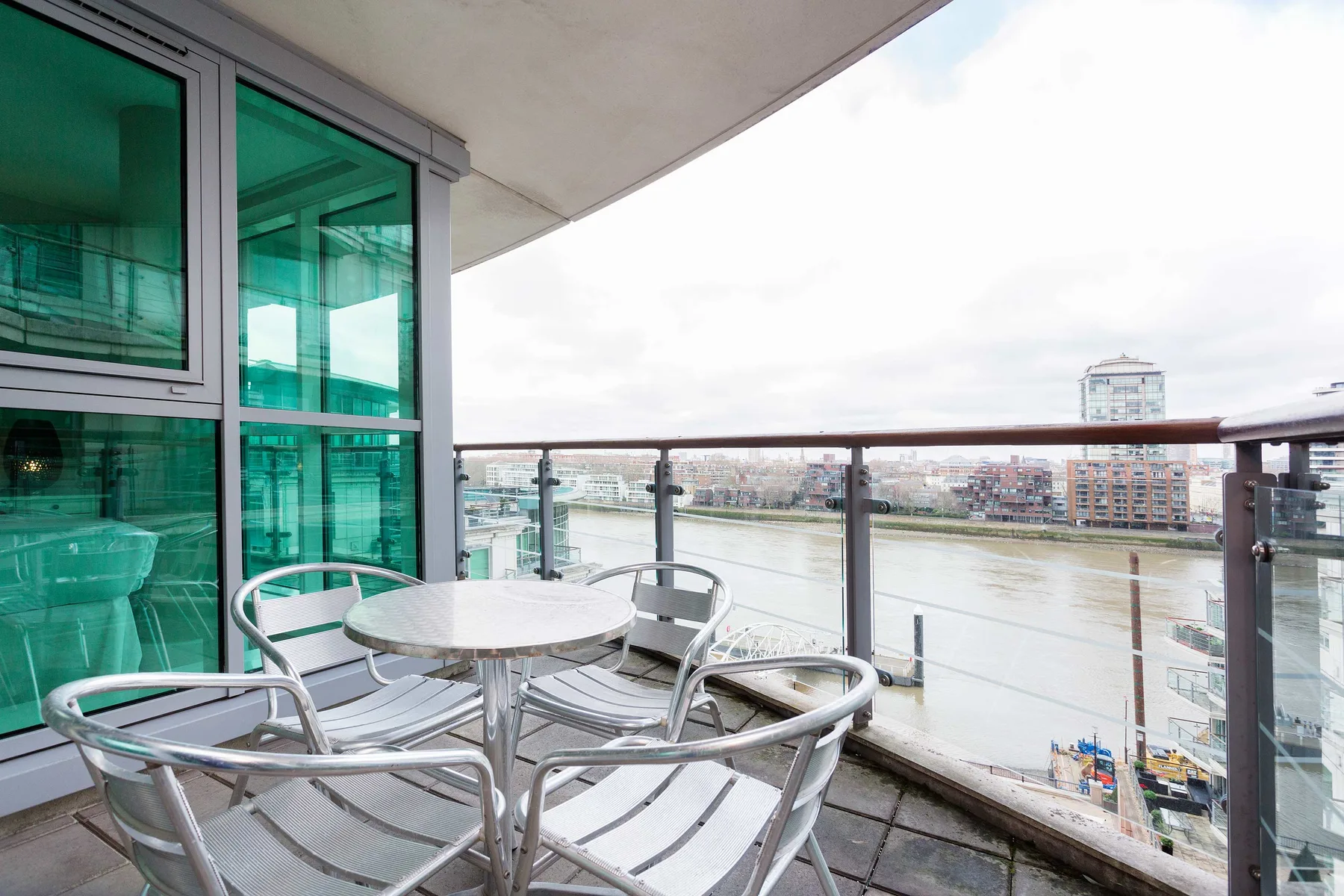 A balcony seating area overlooks a river through a glass railing.