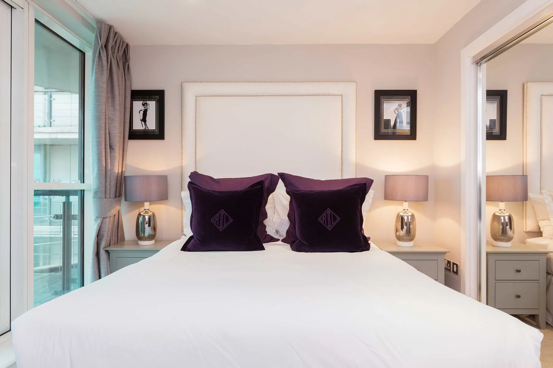 A bedroom with a neatly made bed, dark pillows, and bedside lamps.