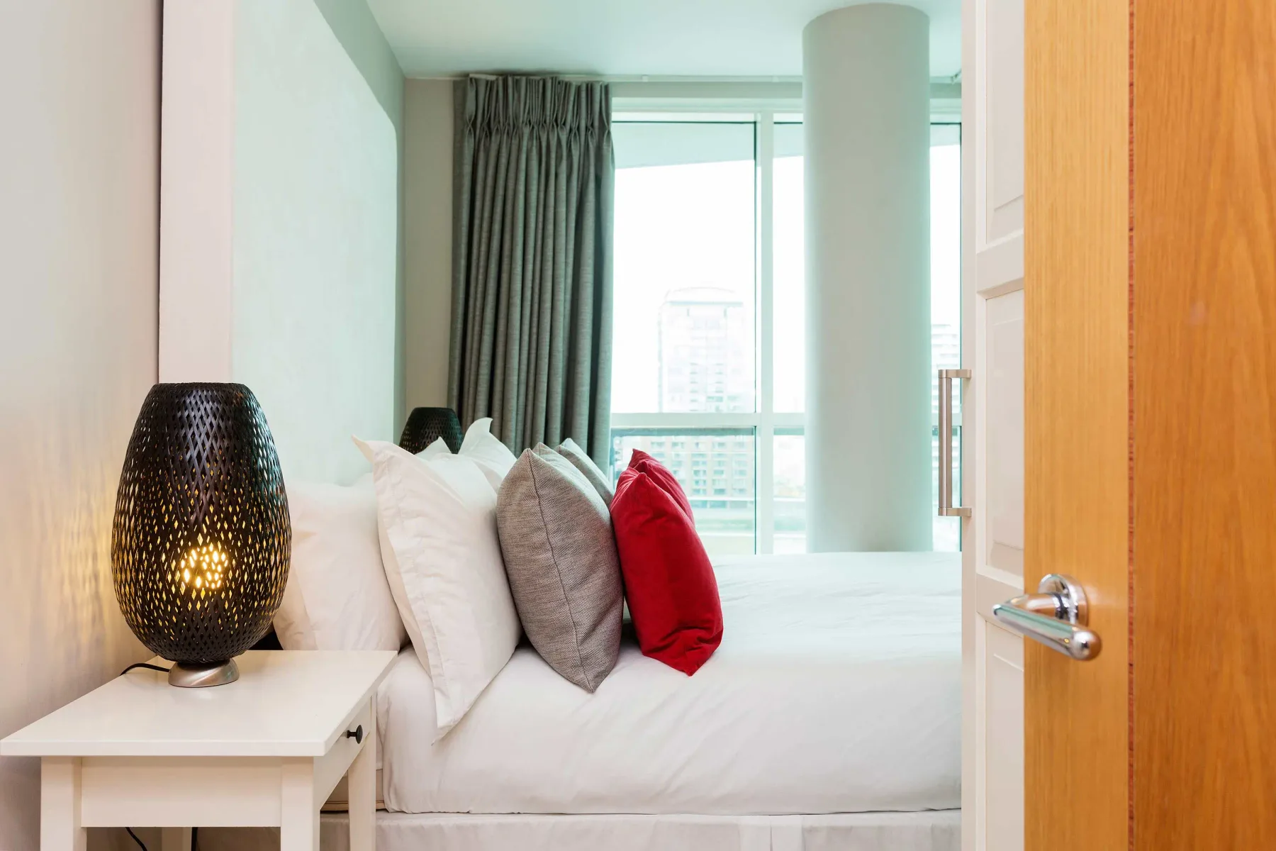 A bedroom with a bed beside a window and an open wooden door.