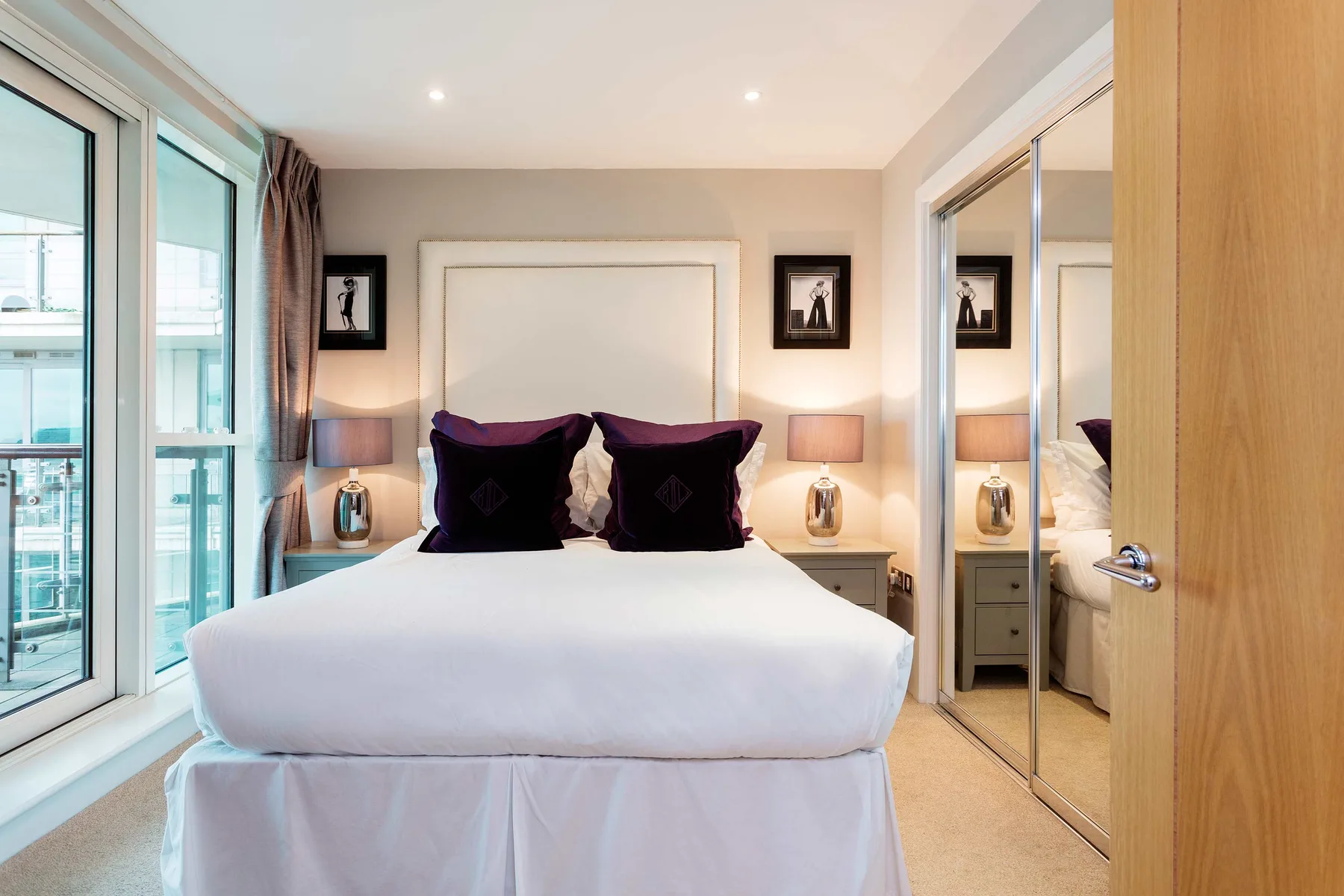 A bedroom with a neatly made bed and large windows.