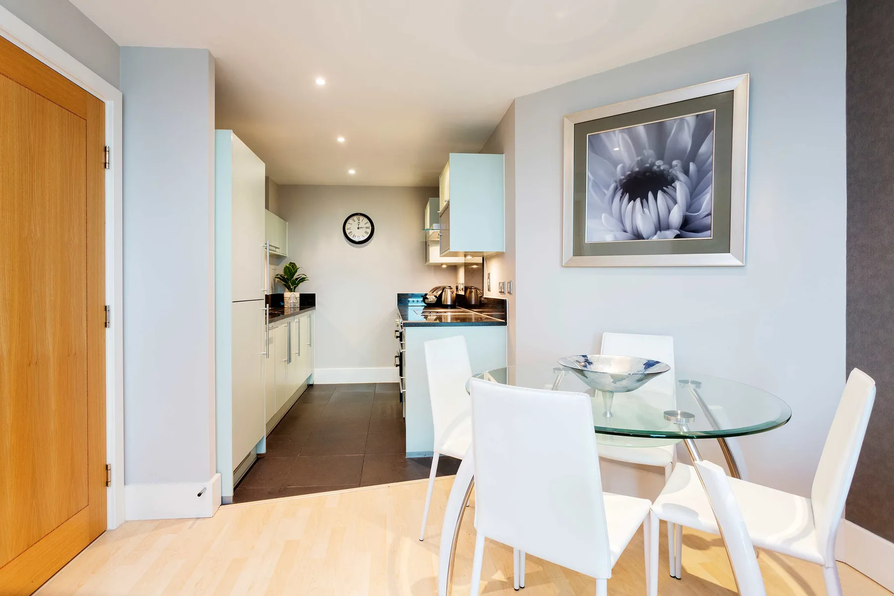 A dining area with a glass table and white seating beside an open kitchen.