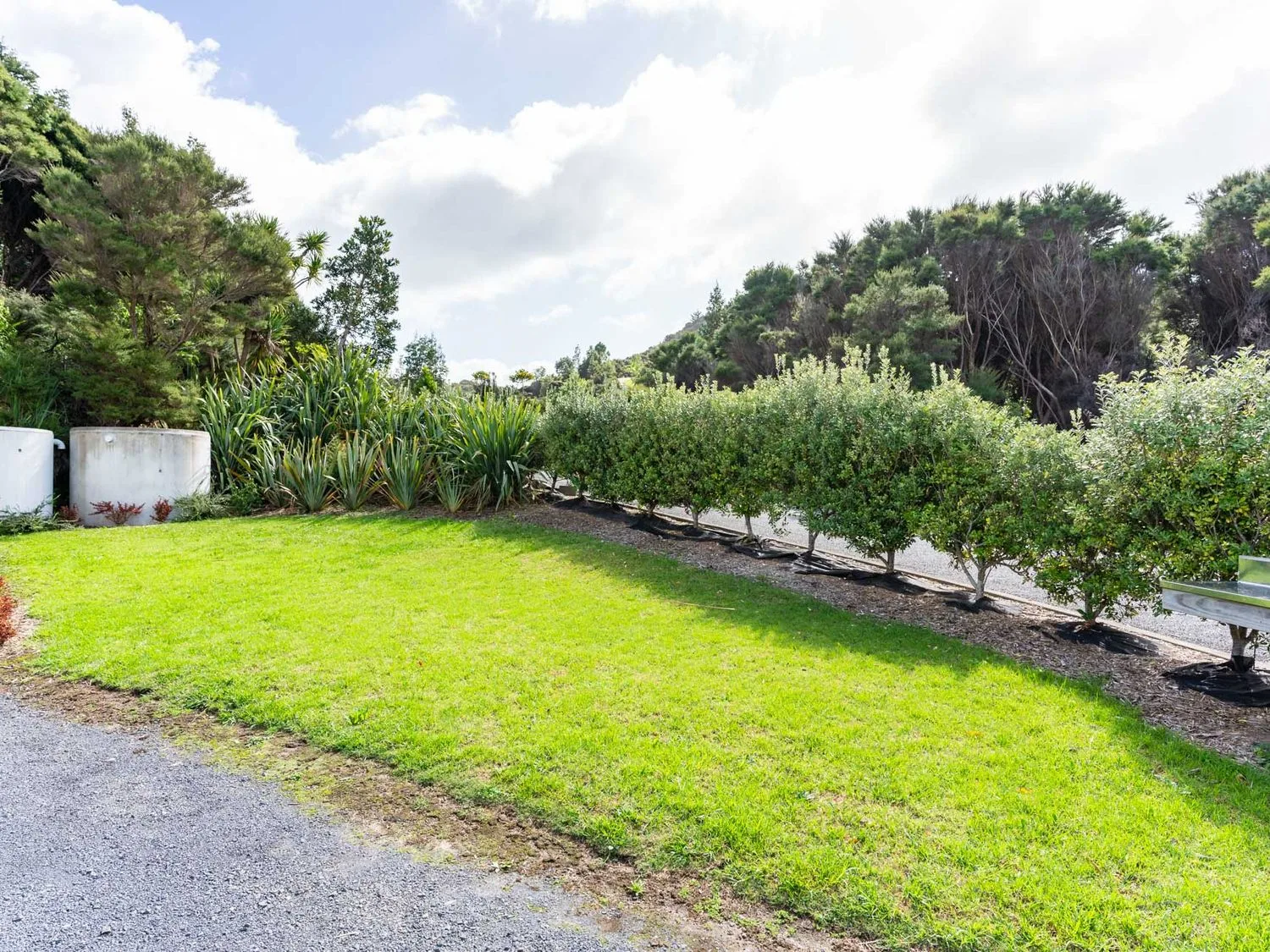 Una zona ajardinada con césped verde y arbustos bordeada por un sendero de grava en Pearls Embrace Mangawhai Heads Studio, en Mangawhai Heads