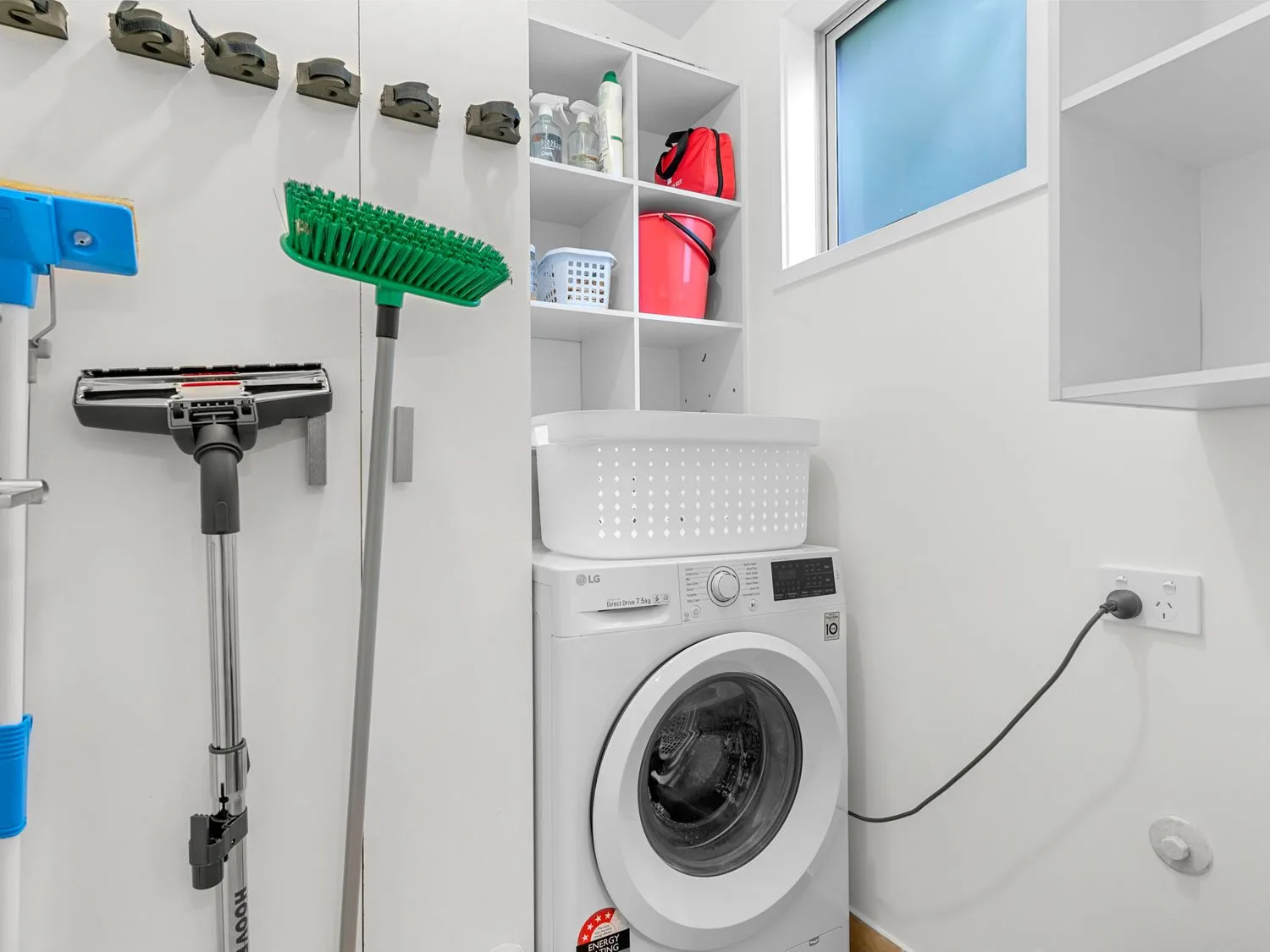 Un cuarto de lavado con una lavadora, utensilios de limpieza y estantes.