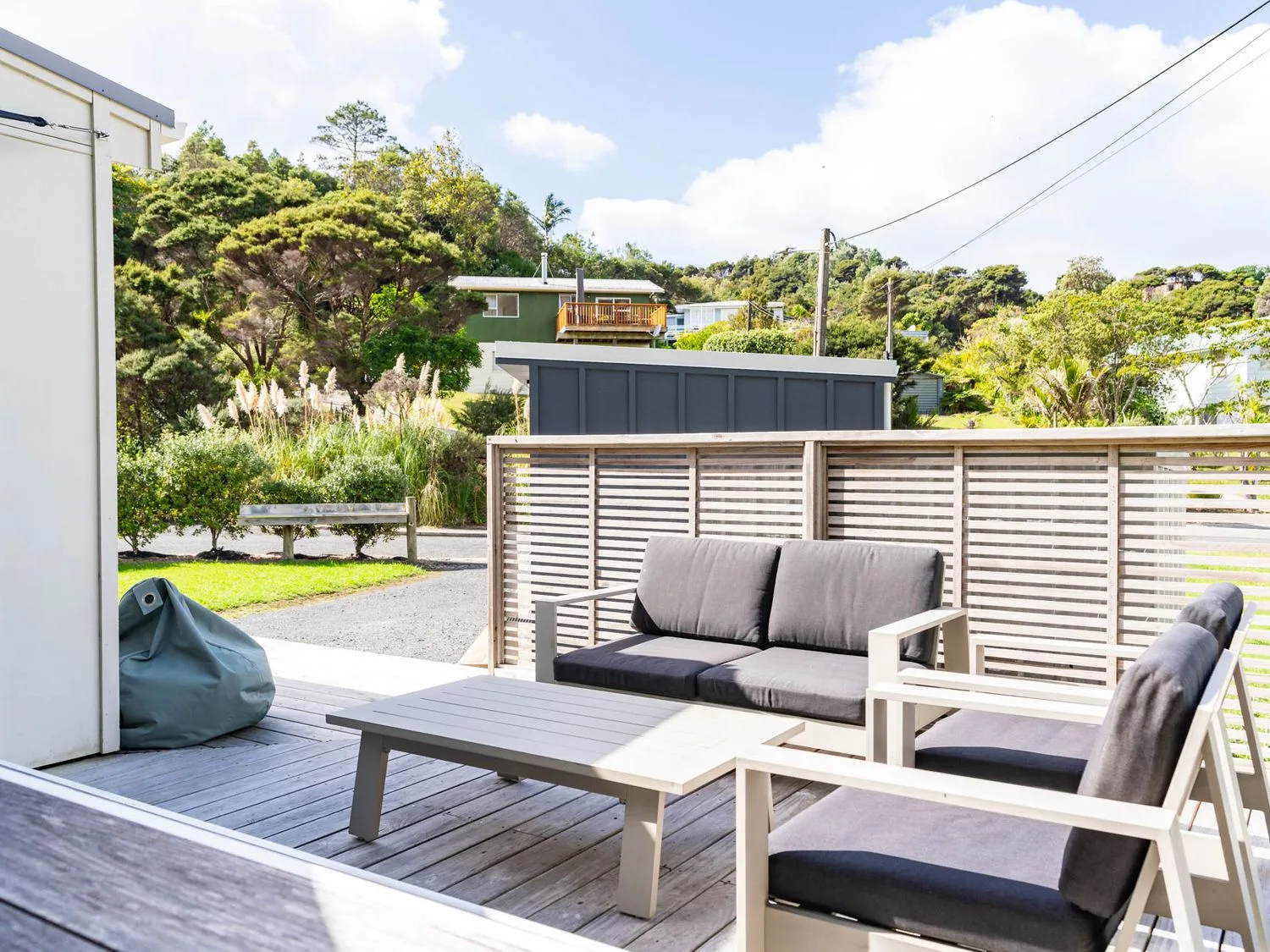 Una terraza exterior con asientos acolchados y una mesa baja, junto a una pantalla de listones.