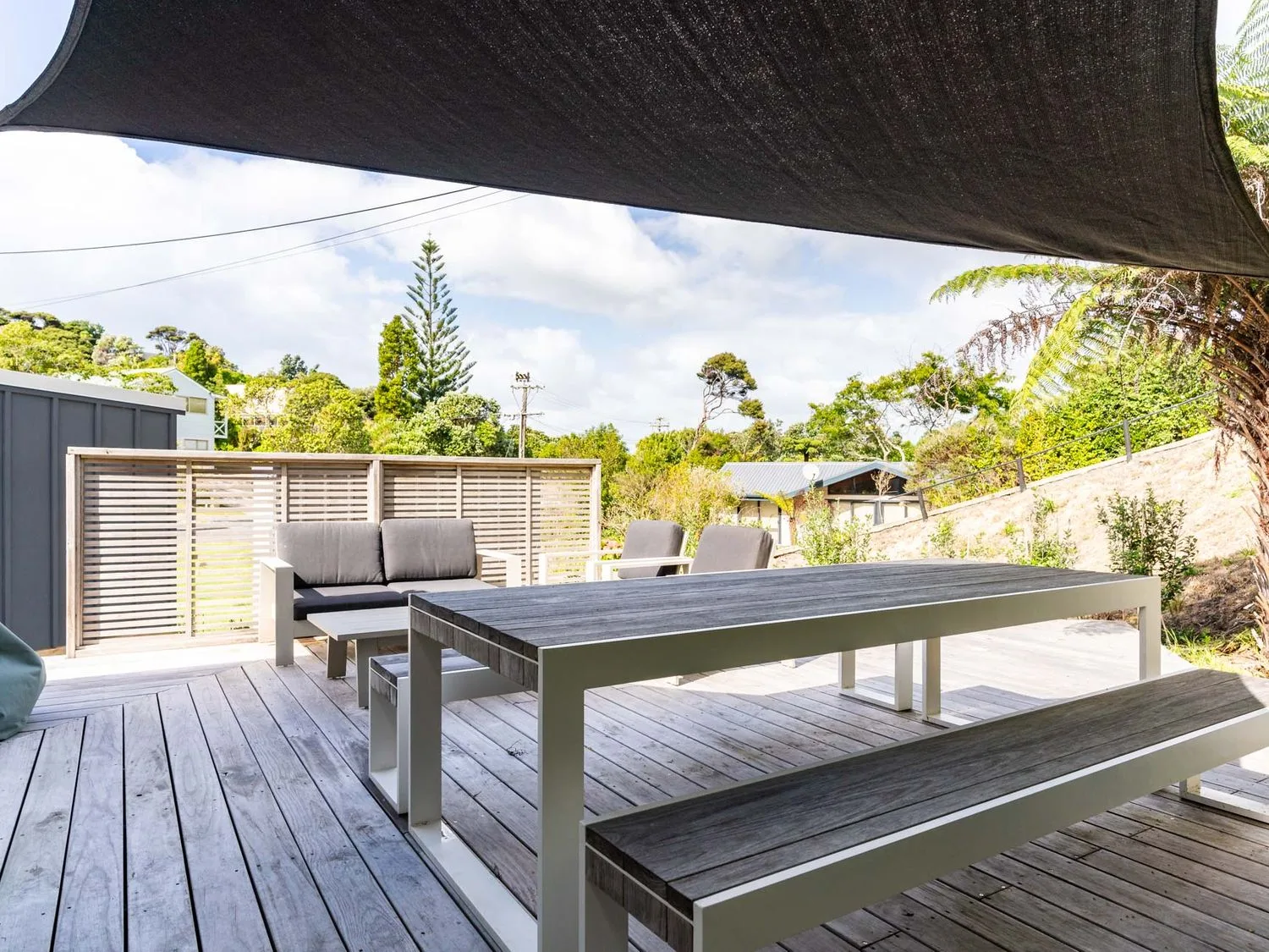 Una terraza exterior con una mesa de comedor y bancos bajo un toldo vela.