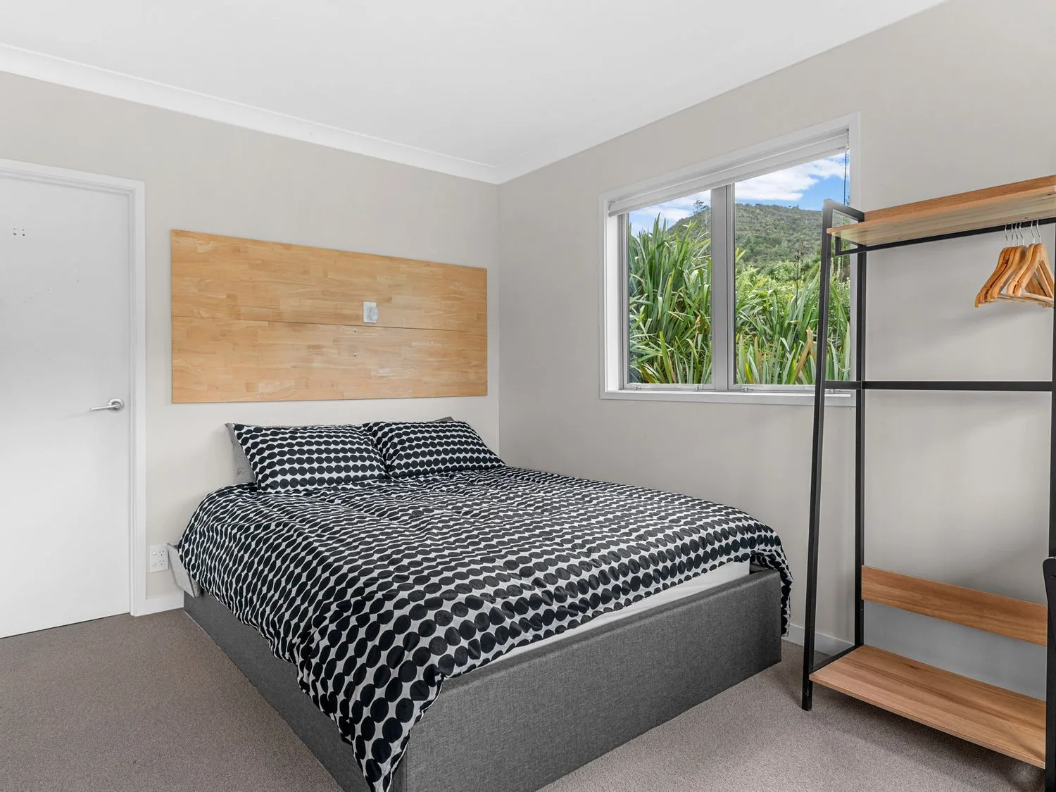 Un dormitorio con una cama de estampado blanco y negro y una ventana con vegetación.