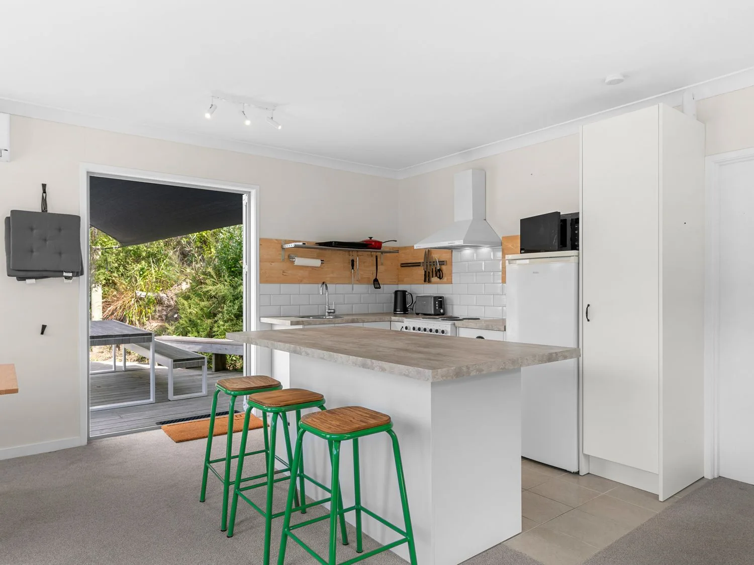 Una cocina con una isla y taburetes verdes, junto a una puerta abierta que da a una terraza.