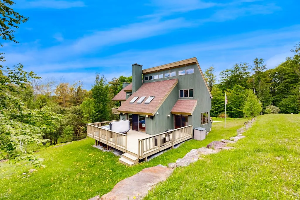 A green house with a raised wooden deck sits beside a grassy yard.
