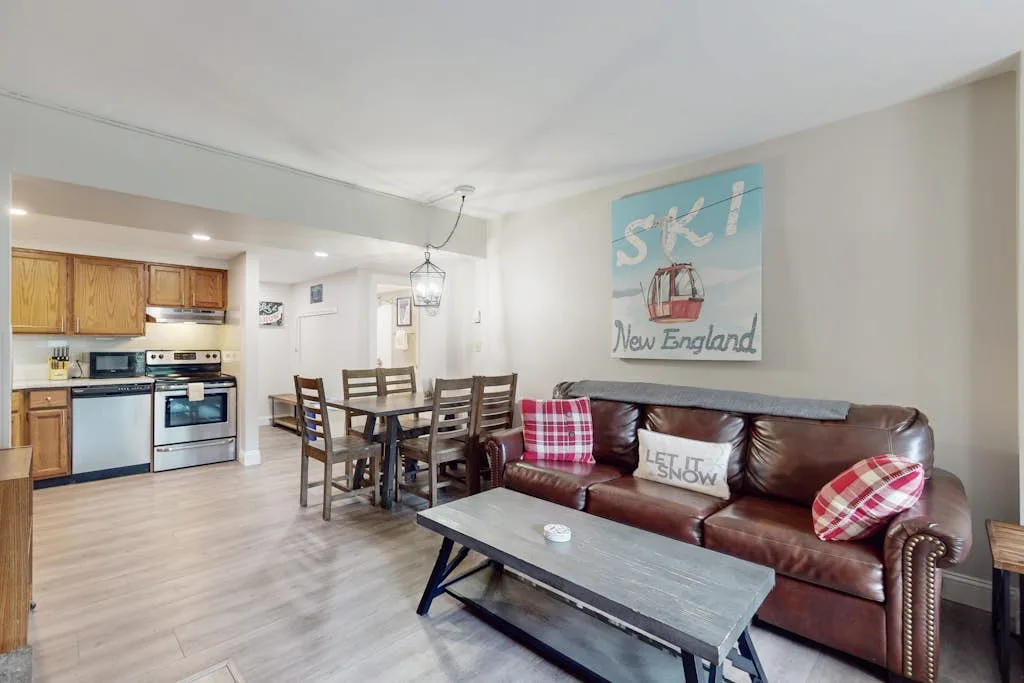 An open-plan living room and kitchen with a dining table and brown leather seating.
