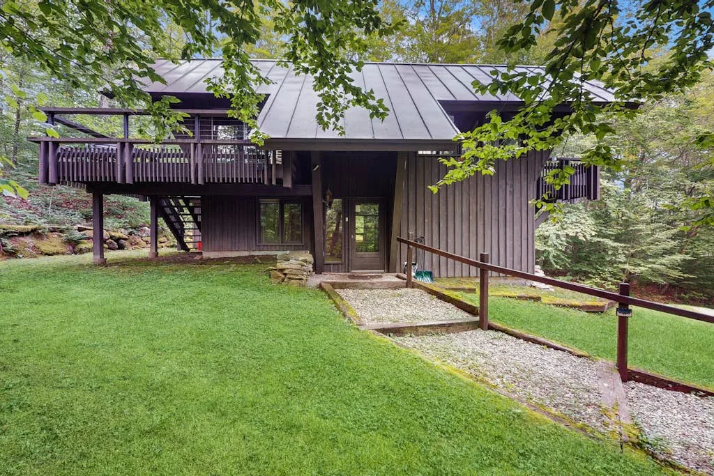 A dark-sided house with a metal roof stands beside a grassy yard.