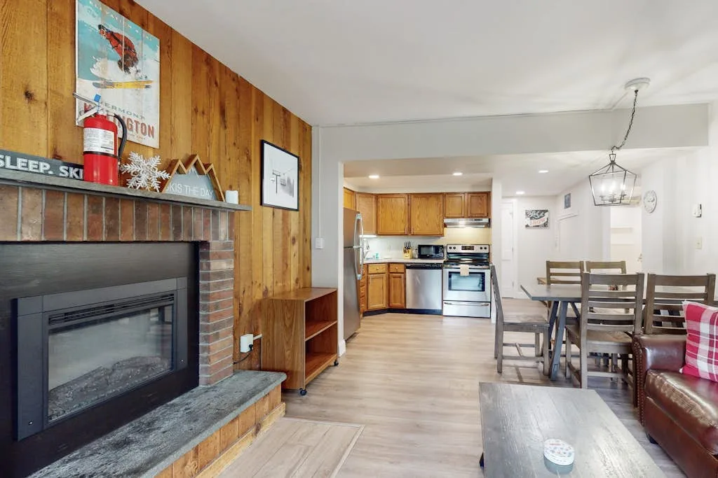 A living and dining area opens into a kitchen, with a fireplace along the wood-paneled wall.