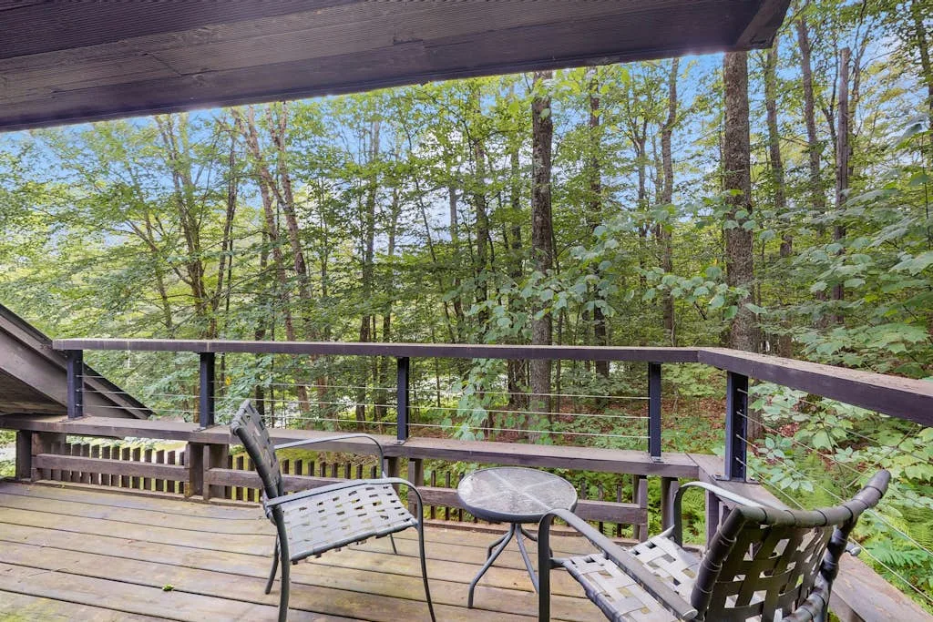 A wooden deck with outdoor seating overlooks a leafy wooded area.