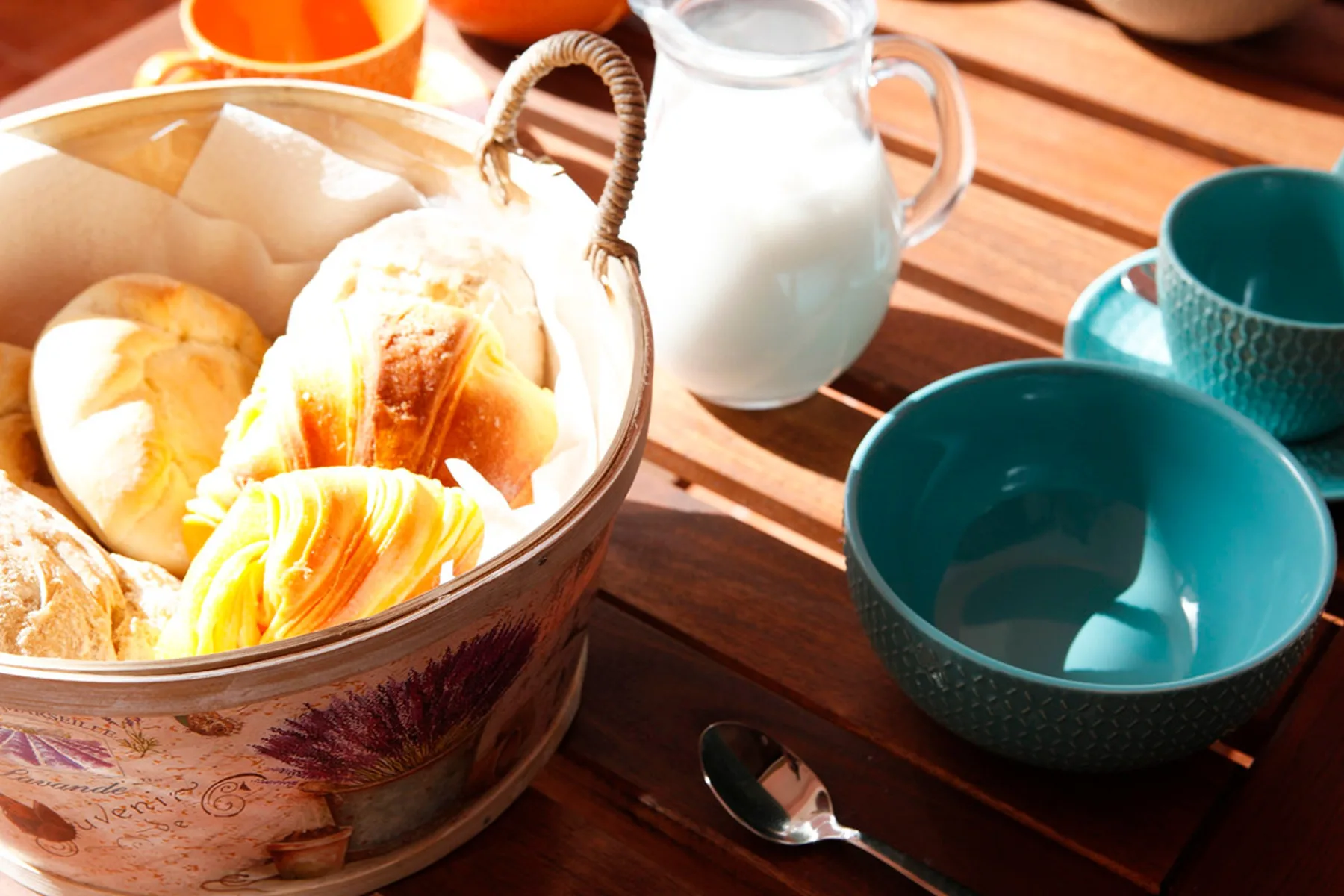 Un desayuno con bollería, una jarra de leche y cuencos sobre una mesa de madera.