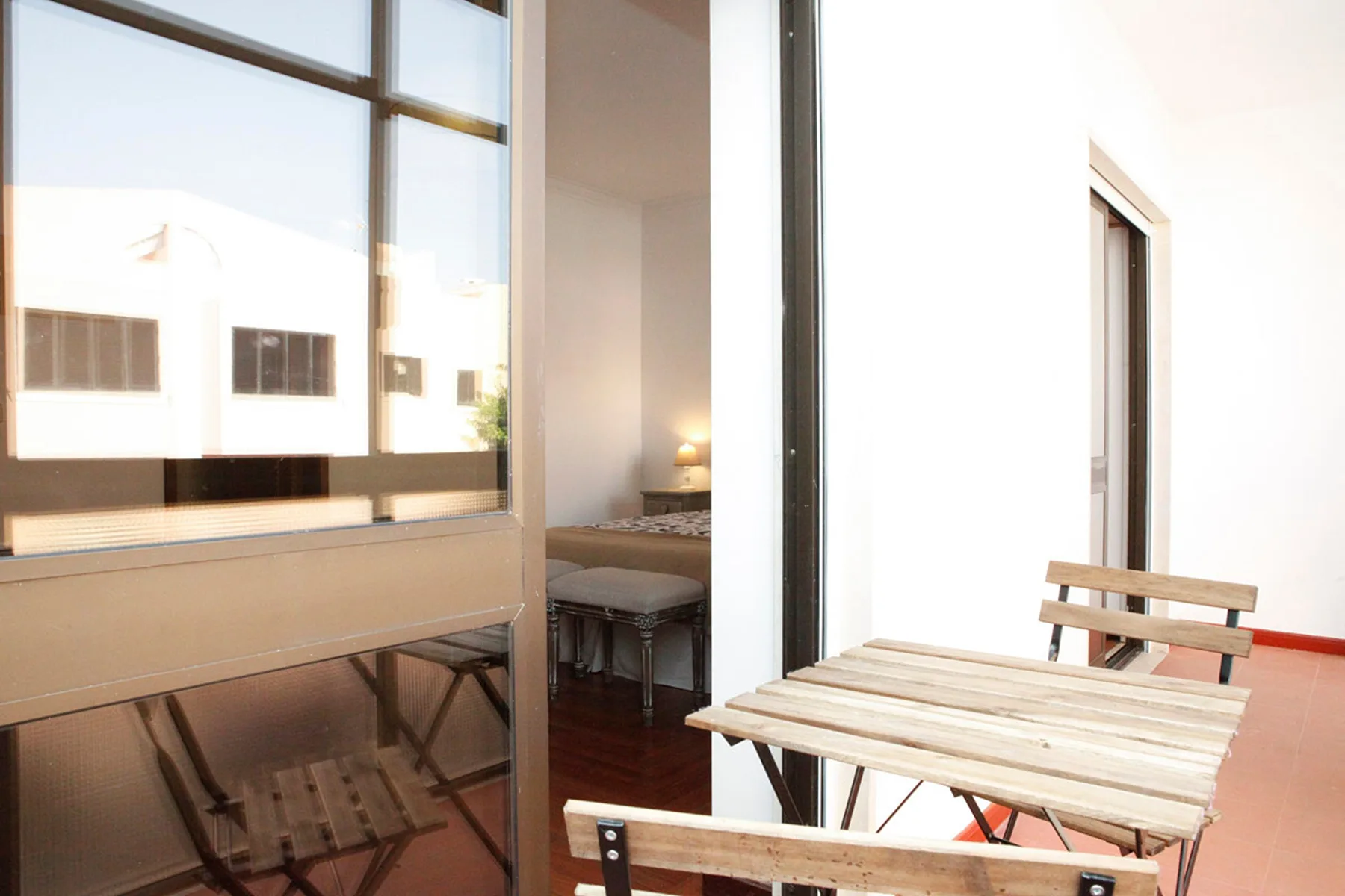 Un balcón luminoso con asientos de madera junto a una ventana grande.