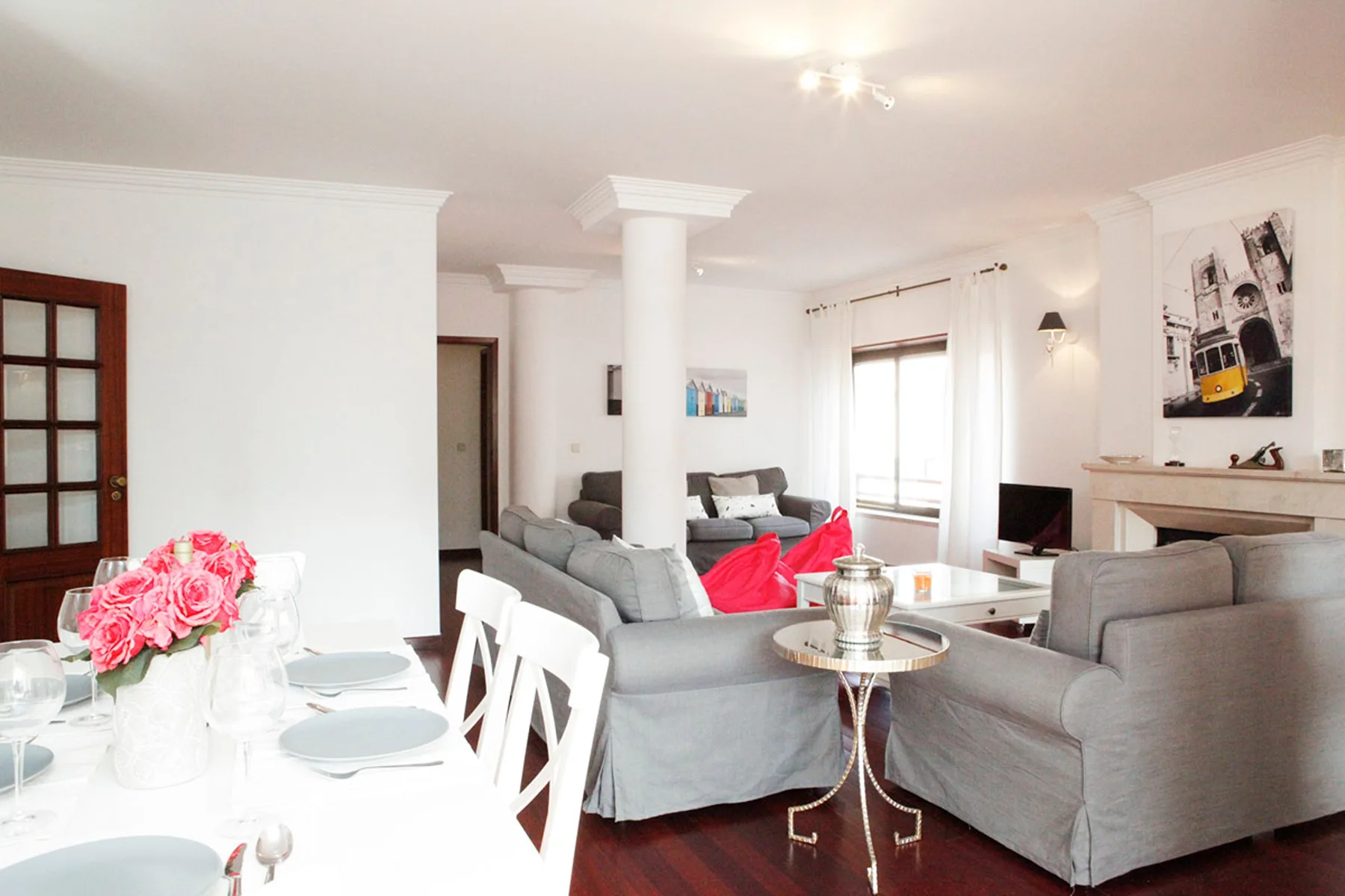 Una luminosa sala de estar y comedor con asientos grises, una mesa blanca y detalles rojos.