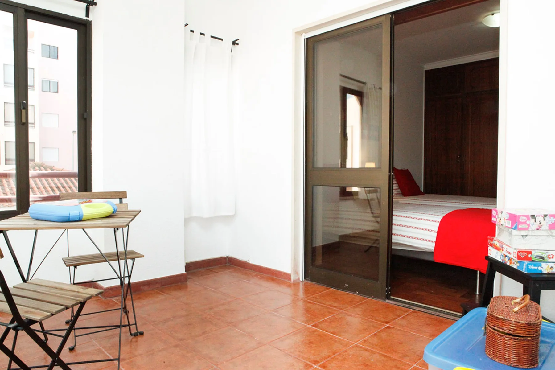 Un dormitorio luminoso se abre a una terraza de baldosas con una pequeña mesa exterior.