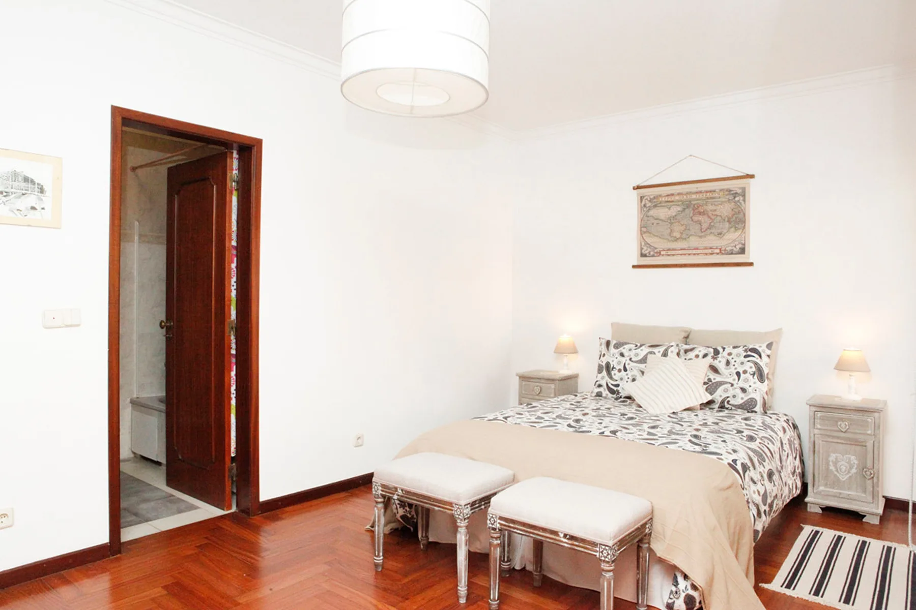 Un dormitorio con una cama, dos taburetes tapizados y suelo de madera.