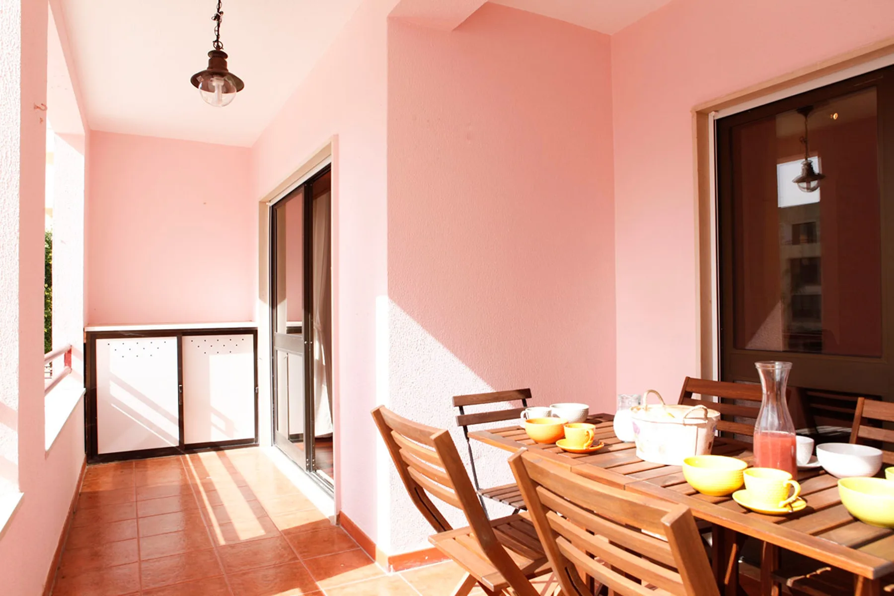 Una zona de comedor soleada con una mesa de madera y sillas en un balcón.