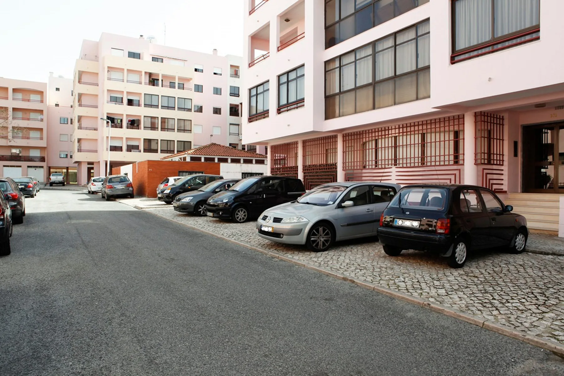 Una zona de estacionamiento pavimentada con varios coches junto a edificios de apartamentos.