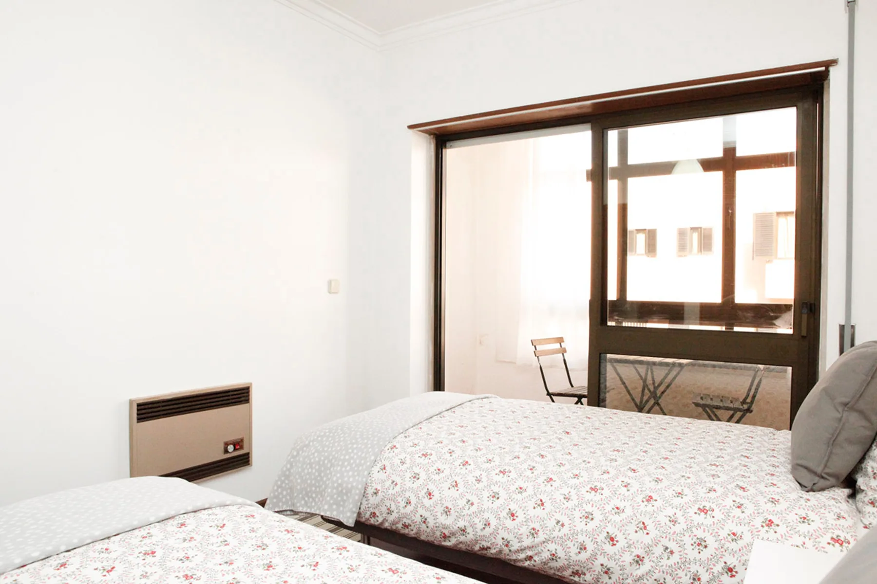 Un dormitorio luminoso con dos camas junto a una ventana grande.