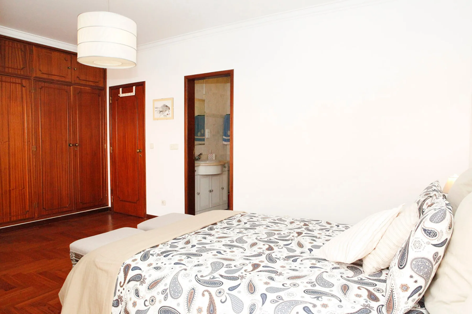 Dormitorio con una colcha estampada junto a un armario de madera.
