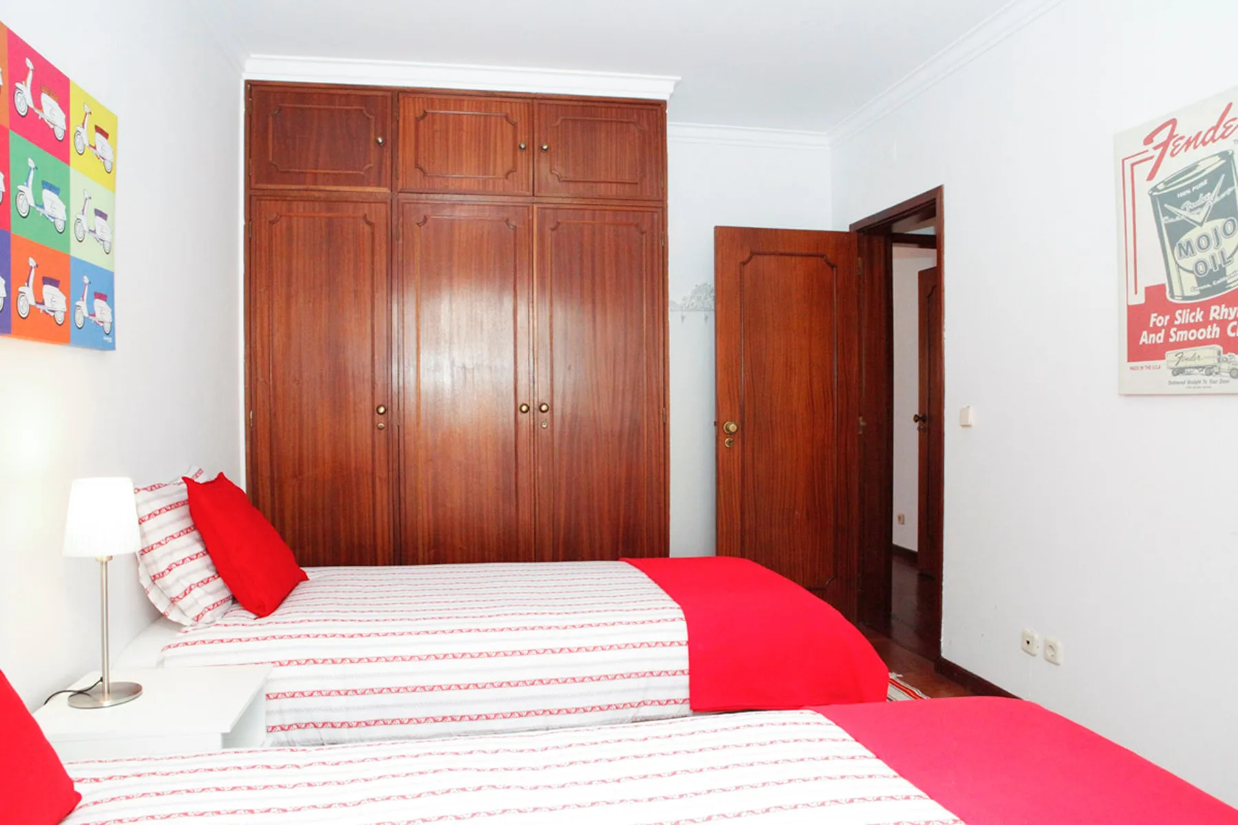 Un dormitorio con dos camas, un armario de madera y arte colorido en la pared.
