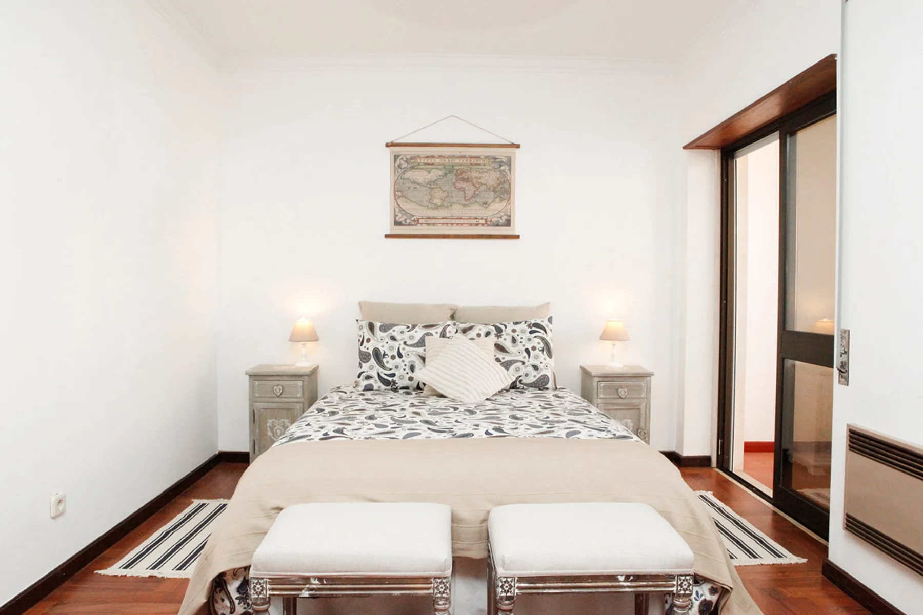 Un dormitorio con una cama estampada y dos bancos tapizados a sus pies.